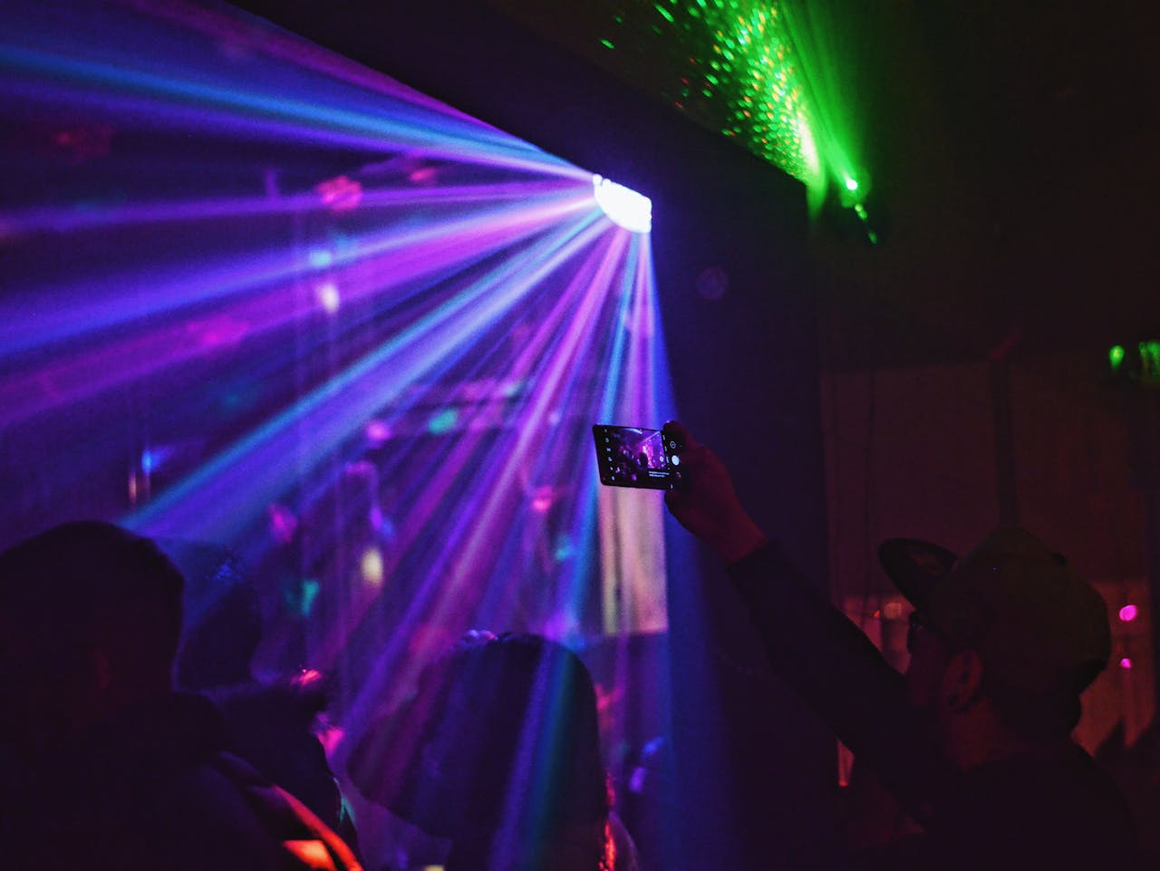 Silhouettes of people in light of disco ball dancing in nightclub and man in cap taking photo